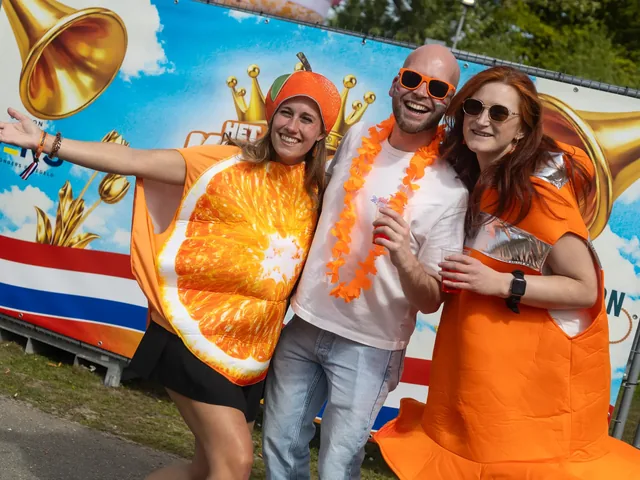 Drie bezoekers in het oranje bij een beschilderde achterwand