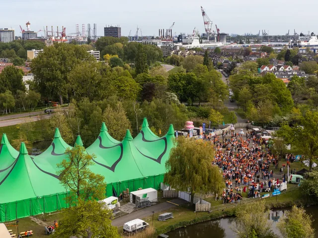 Het festivalterrein van bovenaf, met groene tenten en de stad aan de horizon