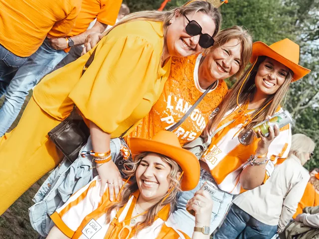 Vier bezoeksters in het oranje, arm in arm