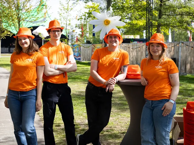 Bezoekers met oranje hoeden aan een statafel tussen grote madeliefdecoraties