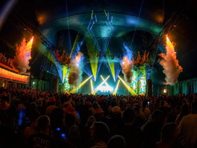 Het hoofdpodium bij avond, met groen en blauw licht en vuurwerk boven het publiek