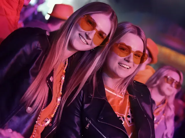 Twee bezoeksters met oranje zonnebrillen in het roze podiumlicht