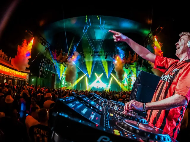 Dj met koptelefoon achter de draaitafels, armen omhoog voor het verlichte podium