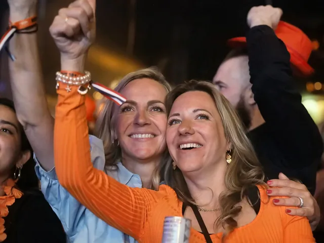 Twee bezoeksters in het oranje juichen met geheven armen